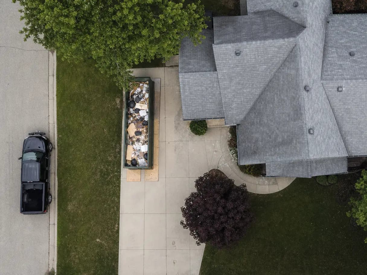 Aerial view of a roll-off dumpster set on plywood along one side of a driveway.